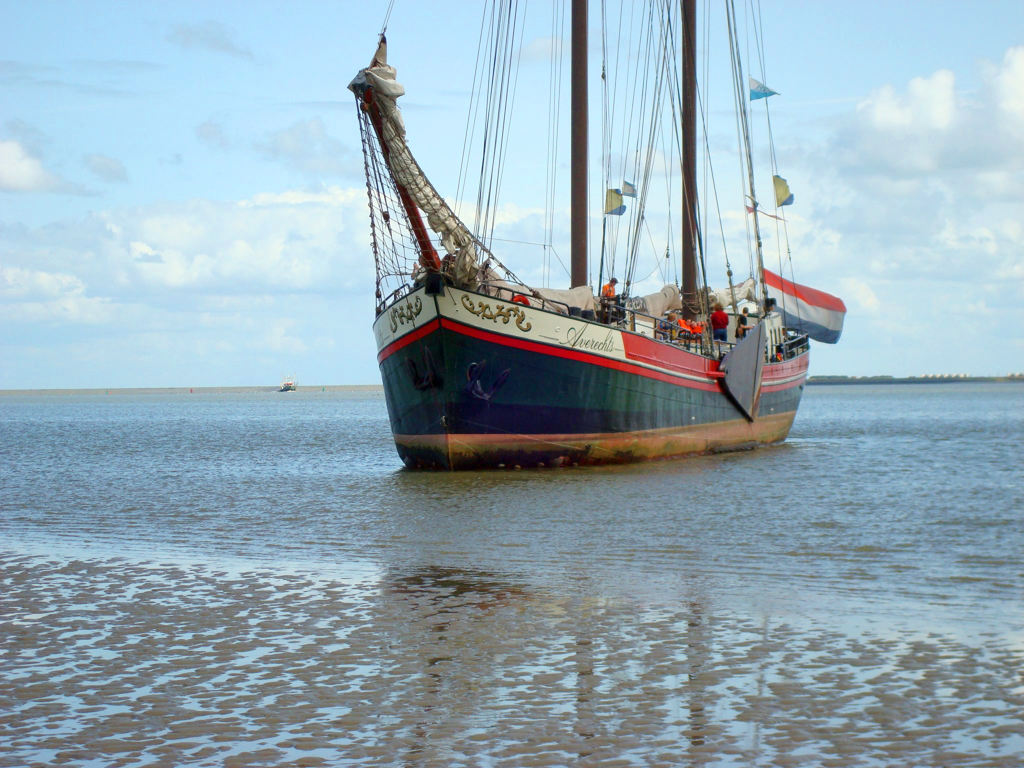 Drooggevallen charterschip op de Waddenzee met zand en water aan een blauw lucht met sluier bewolking