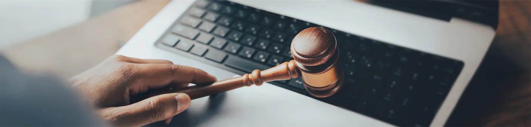 Une main tient un marteau de vente aux enchères au-dessus du clavier d’un ordinateur portable, symbolisant la finalisation d’une enchère en ligne. L’image dégage un sentiment d’autorité et d’intégration technologique.