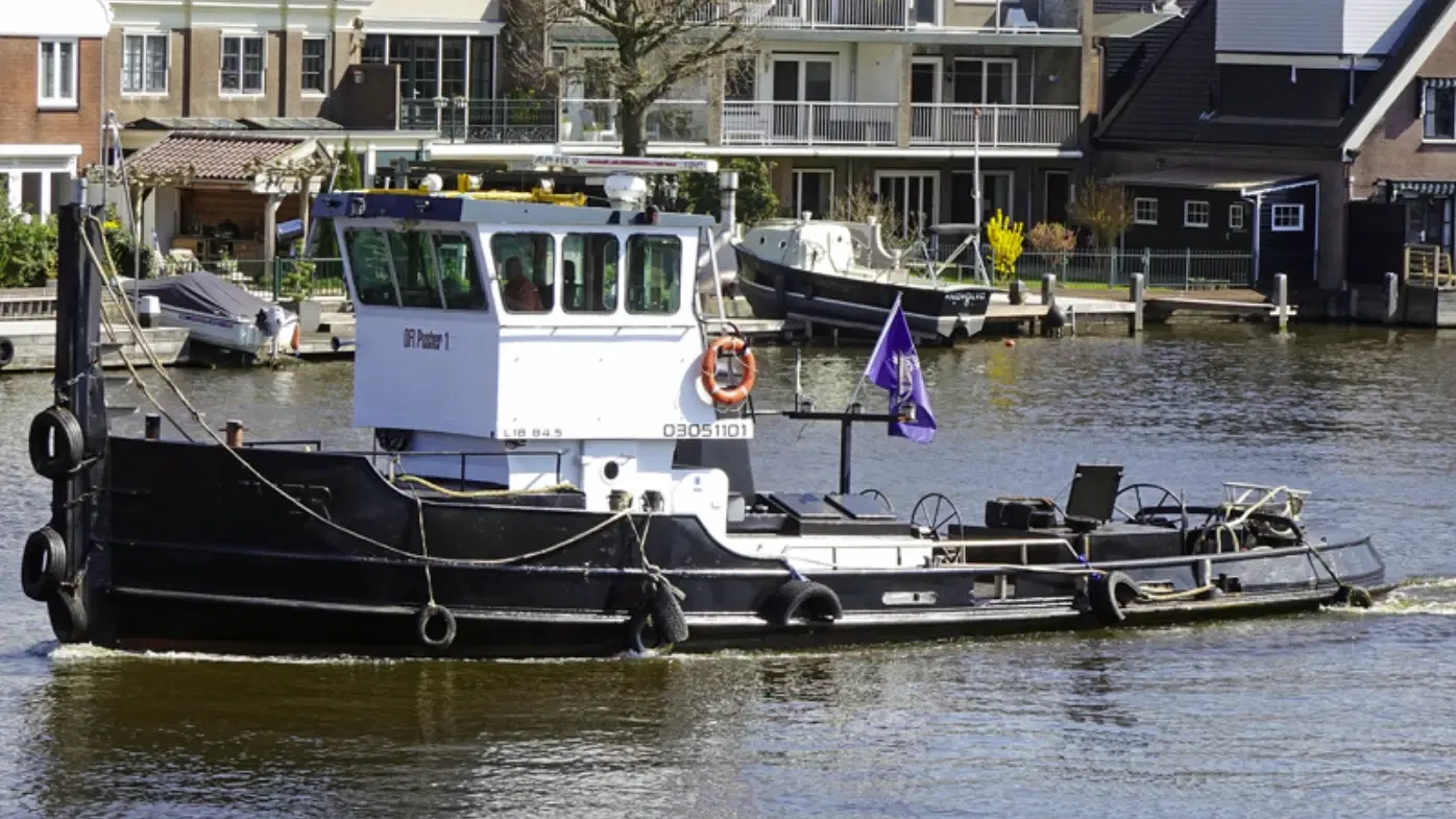 Een duw/sleepboot vaart door rustig water langs huizen